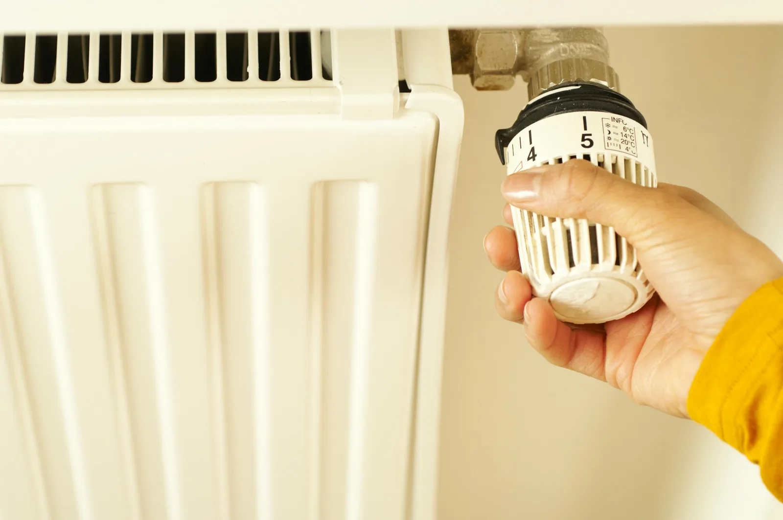 Hand justerar termostat på vit radiator i hemmet